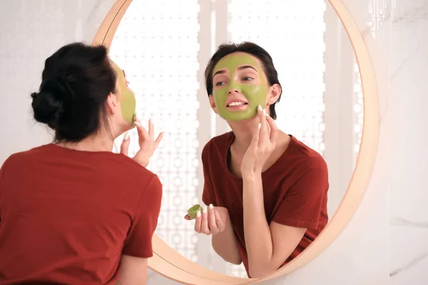 Mladá žena, která používá masku na obličeji blízko zrcadla v koupelně — Stock fotografie