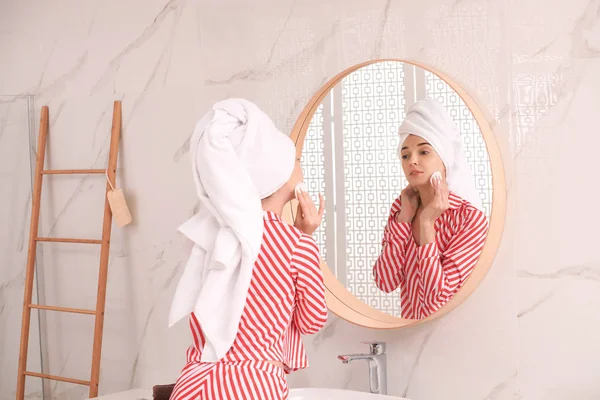 Giovane donna con asciugamano sulla testa vicino specchio in bagno — Foto Stock