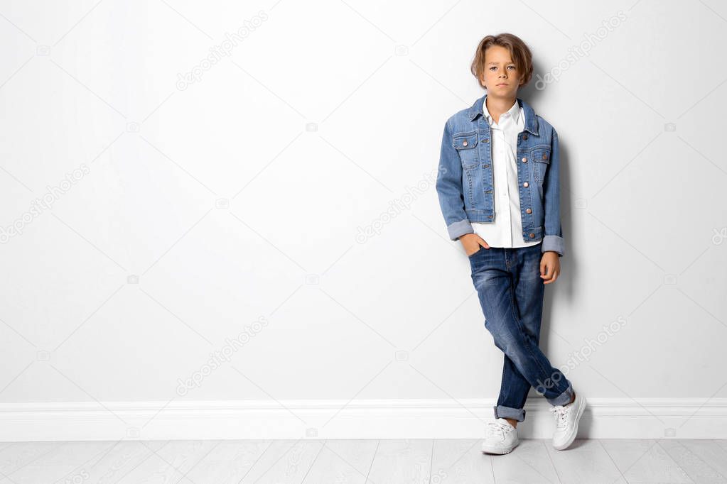 Cute little boy in casual outfit near white wall. Space for text