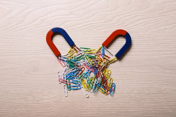 Magnets attracting colorful paper clips on light wooden background, flat lay — Stock Photo, Image