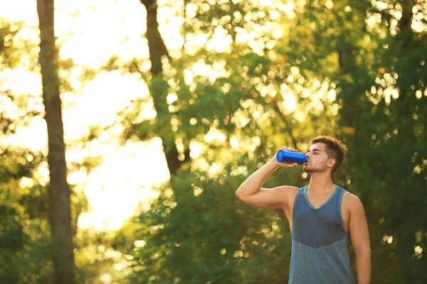 Young man drinking water from sport bottle after training in park — Stock Photo, Image