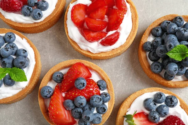 Heerlijke zoete gebakjes met bessen op een grijze tafel, platte lag — Stockfoto