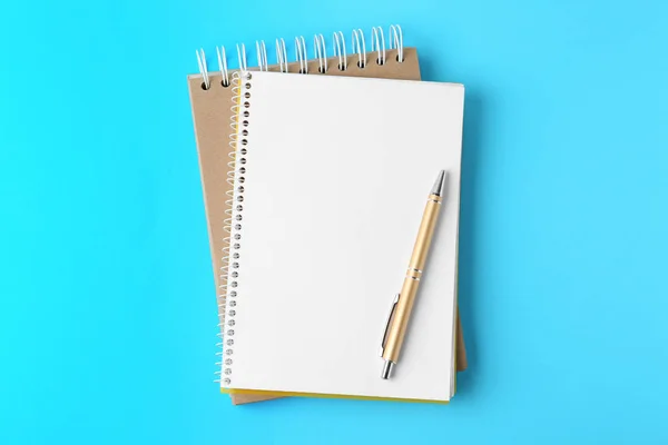Notebooks and pen on light blue background, top view