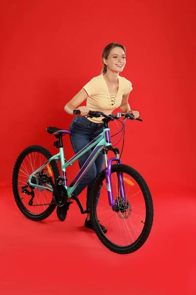 Счастливая молодая женщина с велосипедом на красном фоне — стоковое фото