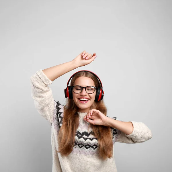 Jonge vrouw luisteren naar muziek met koptelefoon op grijze achtergrond — Stockfoto