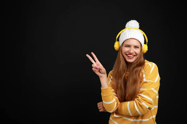 Young woman listening to music with headphones on black background, space for text — Stock Photo, Image