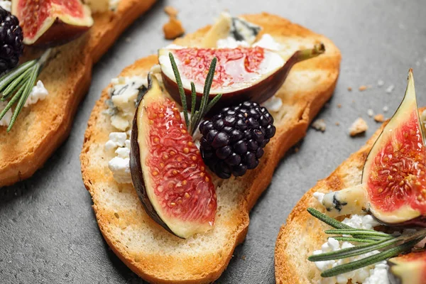 Bruschettas with cheese, figs and blackberries on grey table, closeup