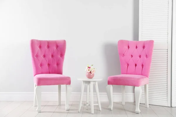 Стильные розовые стулья и стол рядом с белой стеной в комнате — стоковое фото