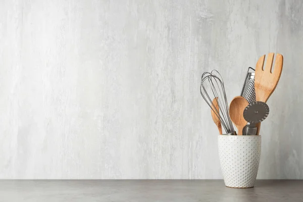 Holder with kitchen utensils on grey table against light background. Space for text — Stock Photo, Image