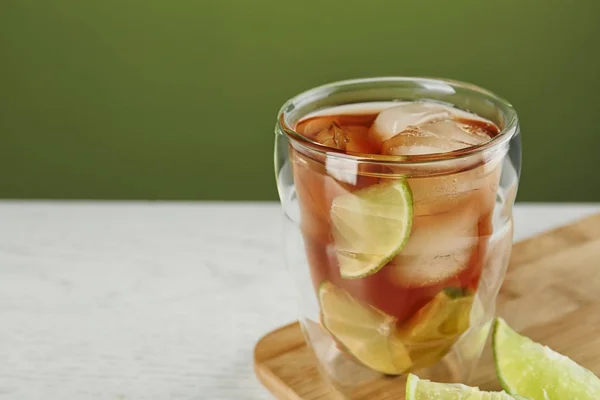 Glas smakelijke ijsthee met limoen op witte houten tafel tegen groene achtergrond, ruimte voor tekst — Stockfoto