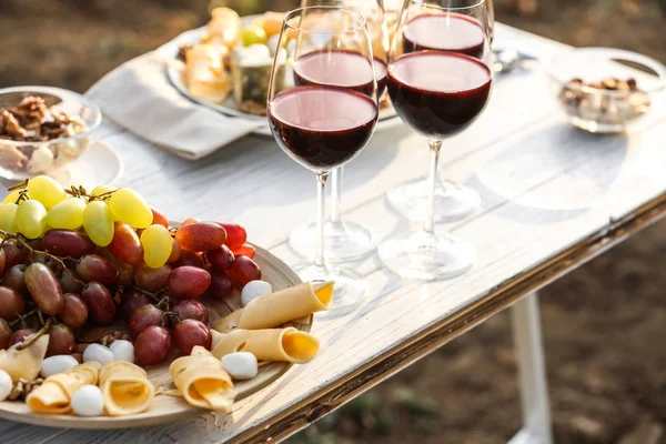 Červené víno a drobné občerstvení podávané pro piknik na bílém dřevěném stole venku — Stock fotografie