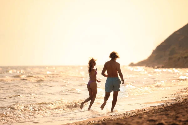 Молодая женщина в бикини и ее парень веселятся на пляже на закате. Прекрасная пара — стоковое фото