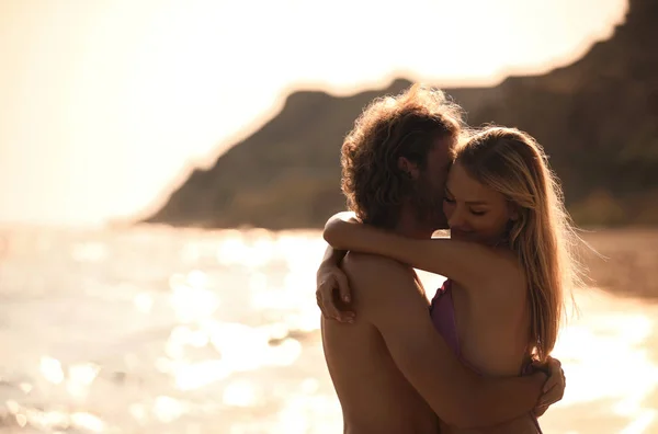 Mujer joven en bikini y su novio en la playa al atardecer. Hermosa pareja. —  Fotos de Stock