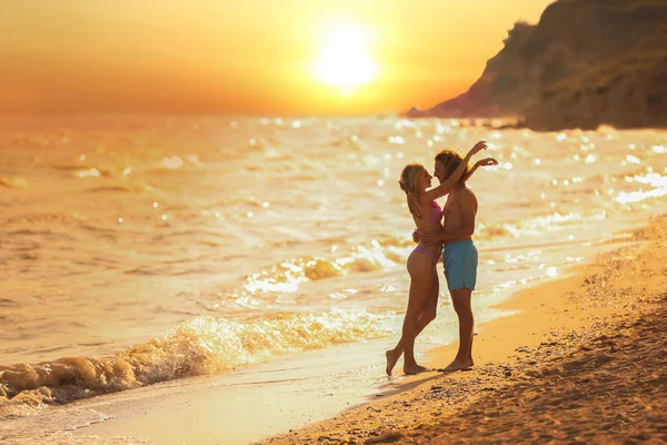 Jovem de biquíni e namorado na praia ao pôr-do-sol. Casal encantador — Fotografia de Stock