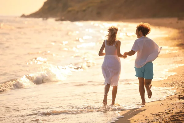 Jeune couple marchant sur la plage au coucher du soleil — Photo