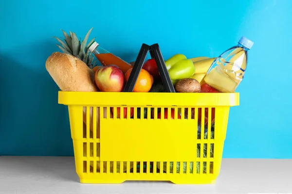 Varukorg med livsmedelsprodukter på vitt bord mot ljusblå bakgrund — Stockfoto