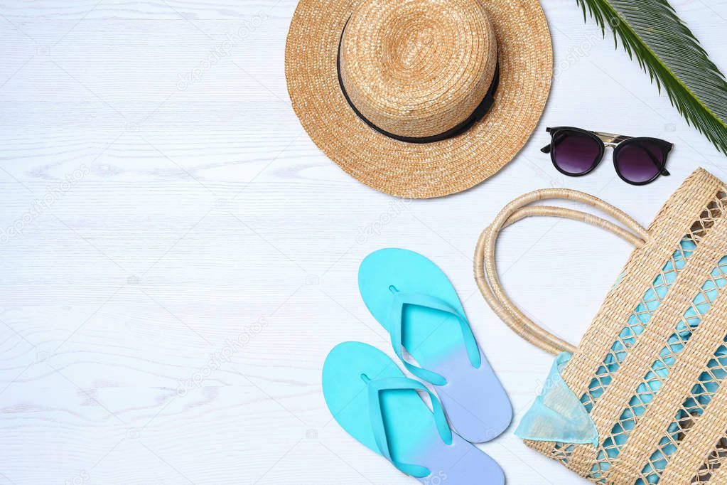 Flat lay composition with beach bag and accessories on white wooden background, space for text