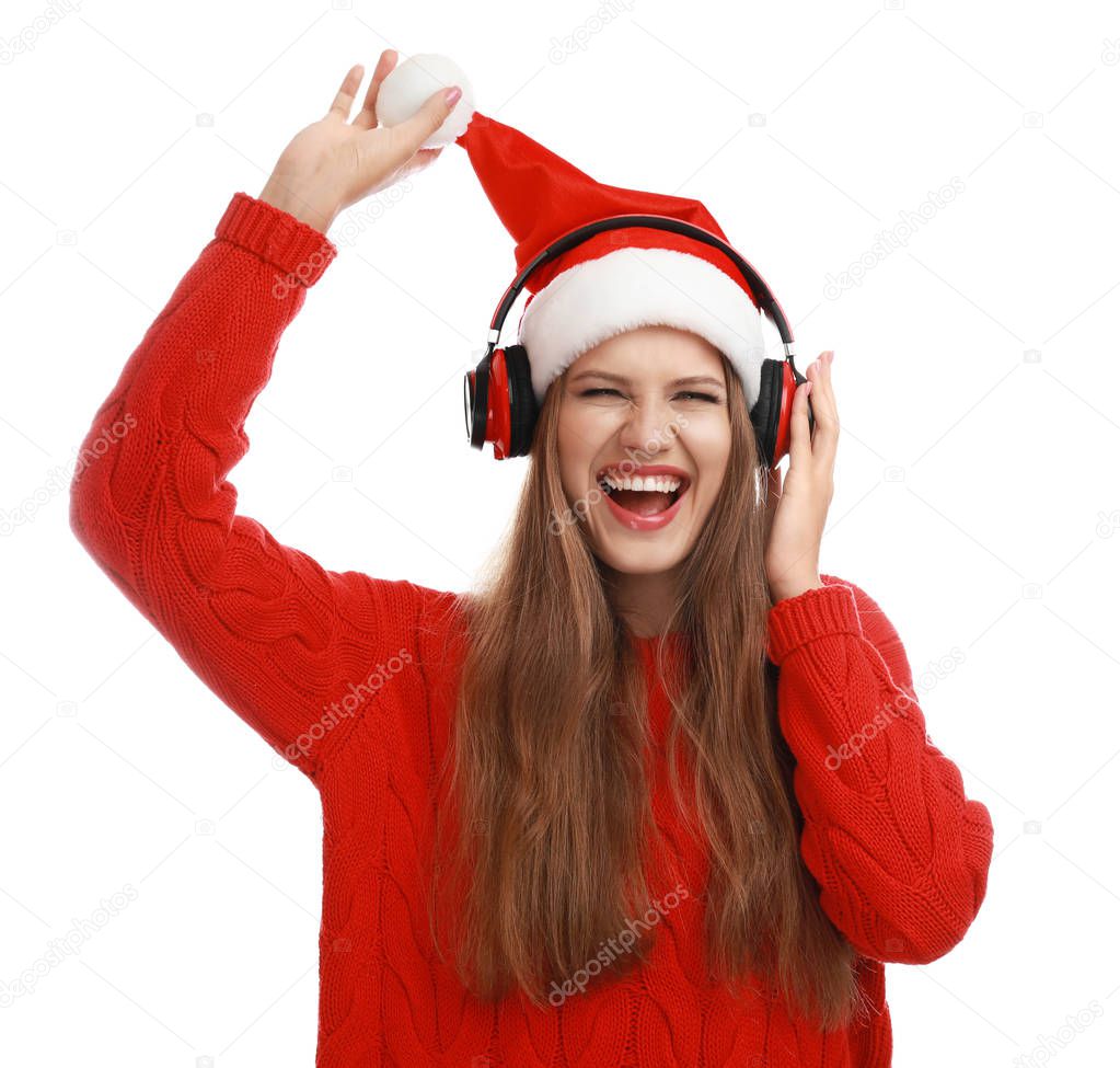 Young woman in Santa hat listening to Christmas music on white background
