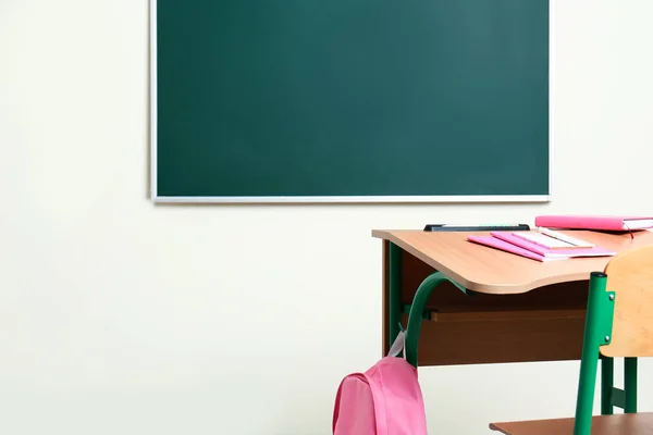 Bureau scolaire en bois avec papeterie et sac à dos près du tableau en classe — Photo