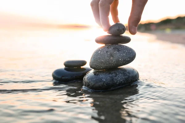 Kvinna stapling mörka stenar på sand nära havet, utrymme för text. Zen Concept — Stockfoto