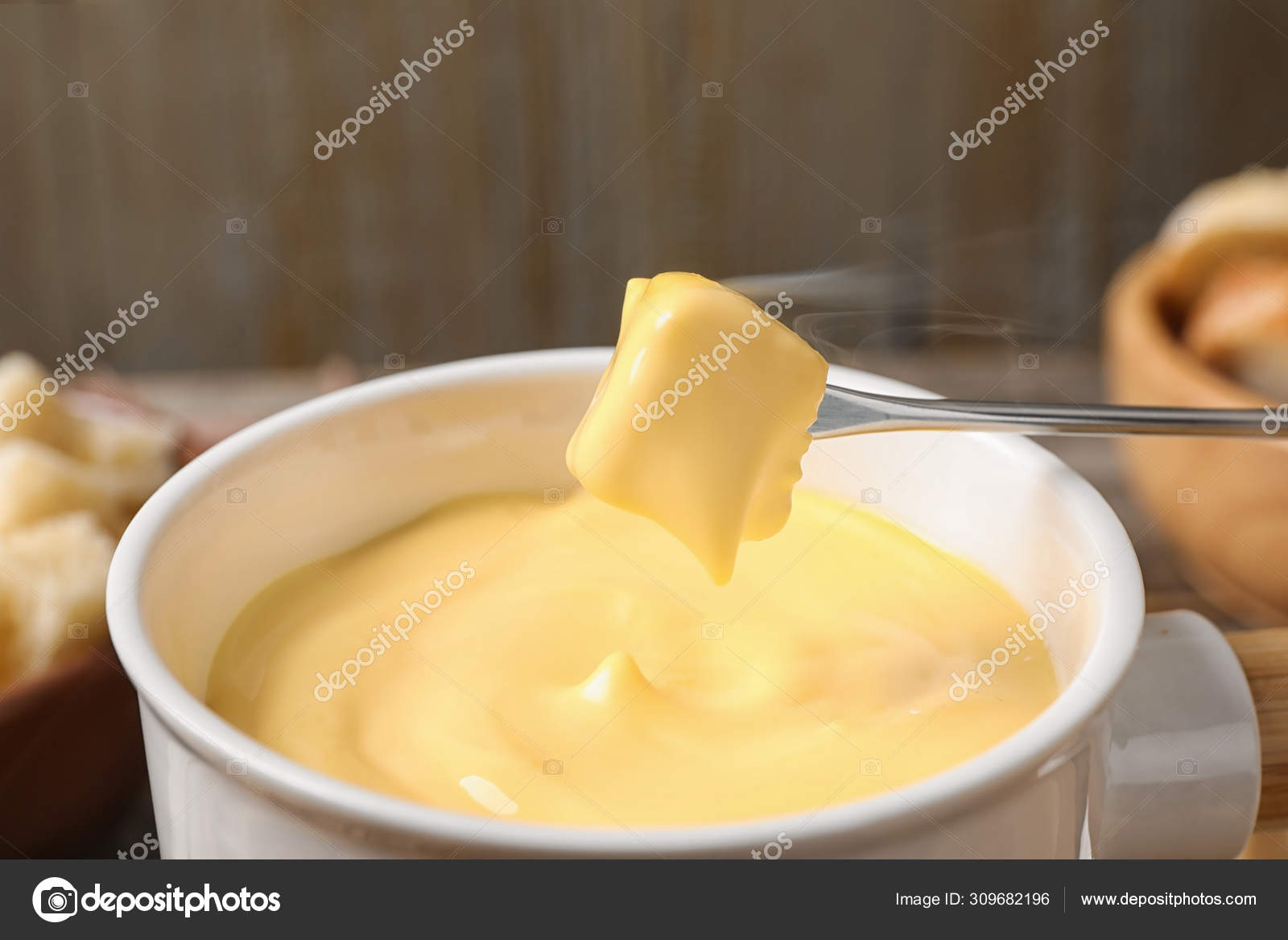 Dipping bread into pot with cheese fondue on table, closeup Stock Photo