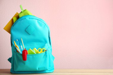 Pembe arka plan karşı ahşap masada farklı okul kırtasiye ile parlak sırt çantası. Metin için alan