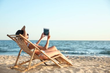 Plajda şezlongda rahatlatıcı tablet ile genç kadın