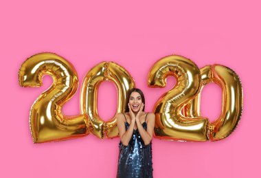 Pembe arka plan üzerinde altın 2020 balonlar yakın Heyecanlı genç kadın. Yeni Yıl kutlaması