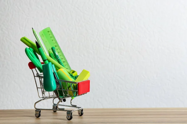 Pequeno carrinho de compras com diferentes artigos de papelaria escolar em mesa de madeira contra fundo branco. Espaço para texto — Fotografia de Stock