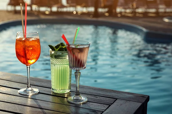 Glasses of fresh summer cocktails on wooden table near swimming pool outdoors. Space for text — Stock Photo, Image