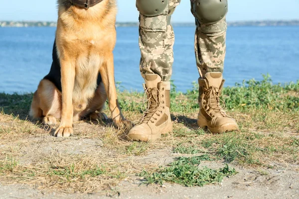 男子身着军装与德国牧羊犬靠近河流，特写视图 — 图库照片