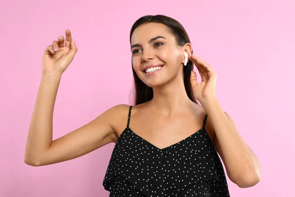 Wanita muda yang bahagia mendengarkan musik melalui earphone nirkabel di latar belakang merah muda — Stok Foto
