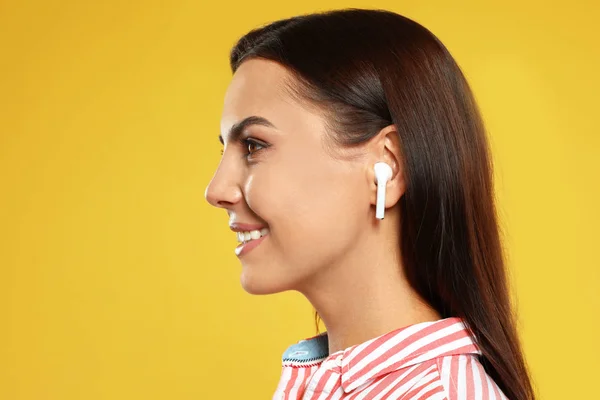 노란색 배경에 무선 이어폰을 통해 음악을 듣고 행복한 젊은 여성 — 스톡 사진