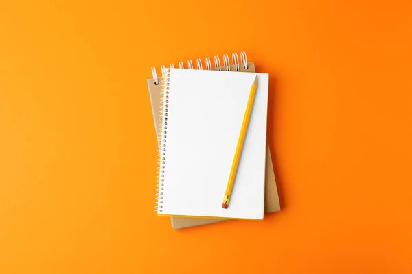 Notizbücher mit Bleistift auf orangefarbenem Hintergrund, Draufsicht — Stockfoto