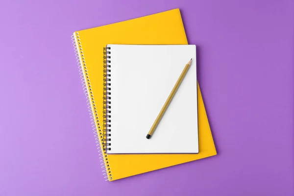 Notebooks with pencil on purple background, top view
