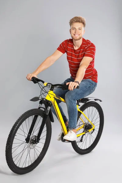 Pohledný mladý muž jedoucí na kole na šedém pozadí — Stock fotografie
