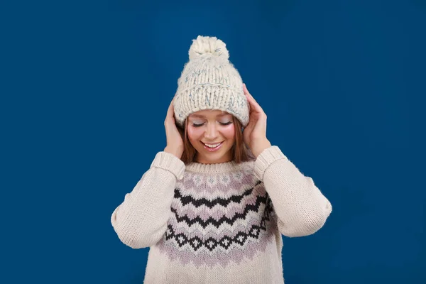 Mujer joven en suéter cálido y sombrero sobre fondo azul. Temporada de invierno — Foto de Stock