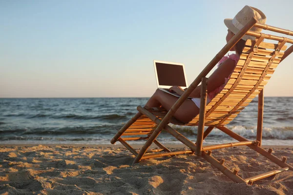 Mujer joven con portátil en la silla de cubierta en la playa — Foto de Stock