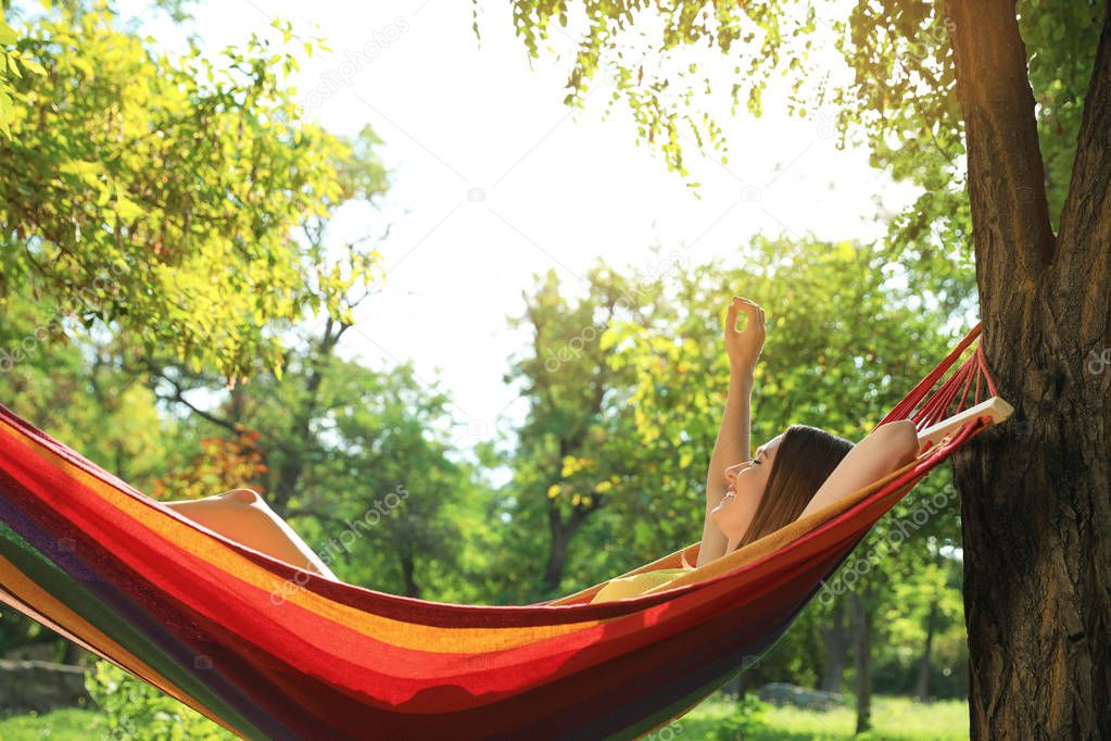 Young woman resting in comfortable hammock at green garden