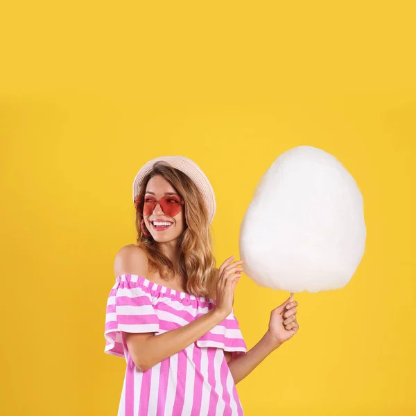 Mujer joven feliz con algodón de azúcar sobre fondo amarillo — Foto de Stock