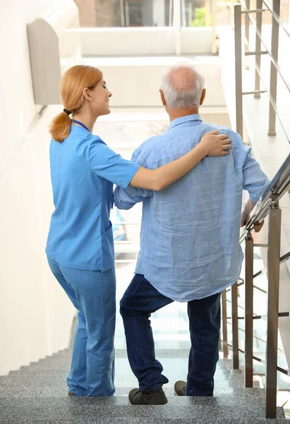 Νοσοκόμα βοηθώντας ηλικιωμένο άντρα σε σκάλες σε εσωτερικούς χώρους — Φωτογραφία Αρχείου