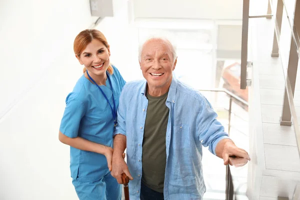 Νοσοκόμα βοηθώντας ηλικιωμένο άντρα σε σκάλες σε εσωτερικούς χώρους — Φωτογραφία Αρχείου