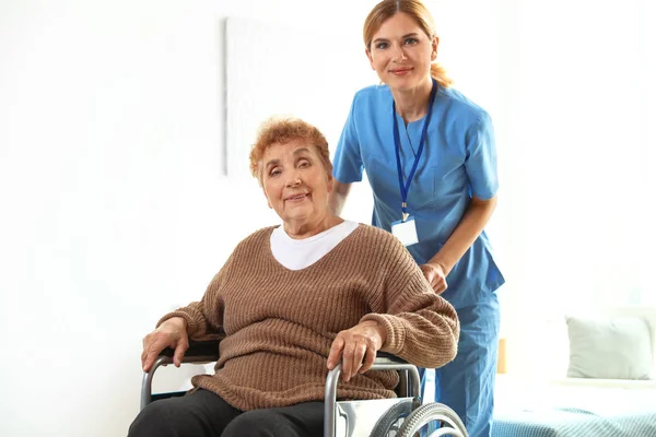 Νοσοκόμα βοηθώντας ηλικιωμένη γυναίκα σε αναπηρικό αμαξίδιο σε εσωτερικούς χώρους — Φωτογραφία Αρχείου