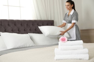 Yatakta çiçek ve otel odasında bulanık oda hizmetçisi ile temiz havlu yığını, closeup. Metin için alan