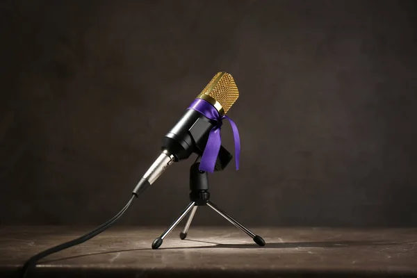 Microphone with purple awareness ribbon on wooden table against dark background