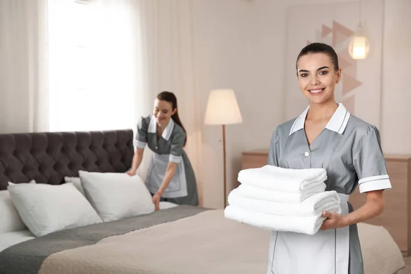 Camareira com pilha de toalhas frescas no quarto de hotel. Espaço para texto — Fotografia de Stock