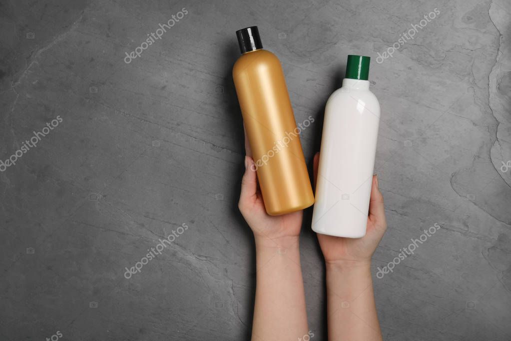 Woman holding blank bottles of cosmetic products on black background, top view. Space for design