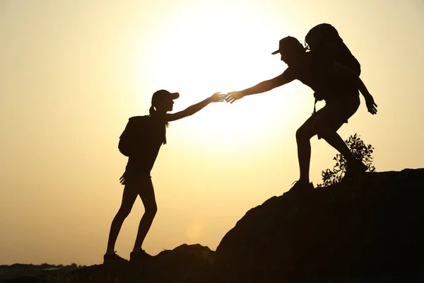 Silhuetter av man och kvinna hjälper varandra att klättra på kullen mot solnedgången — Stockfoto