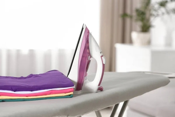 Modern electric iron and clean folded clothes on board indoors
