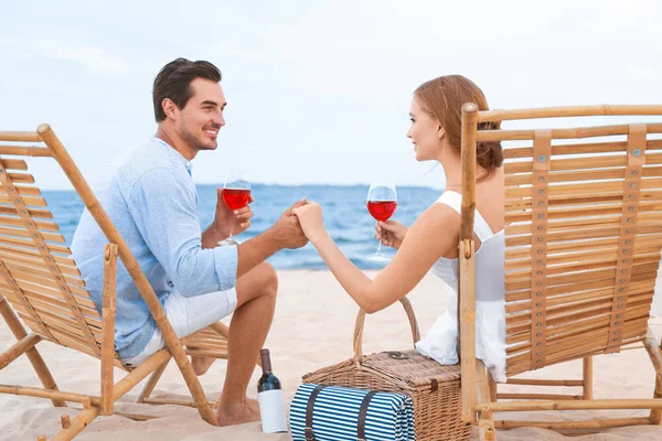 Glückliches junges Paar mit Weingläsern auf Liegestühlen am Meeresstrand — Stockfoto